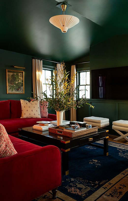 The deep green paint color on the walls and ceiling of the movie room complements the custom sectional the couple designed and also helps camouflage the large TV.
